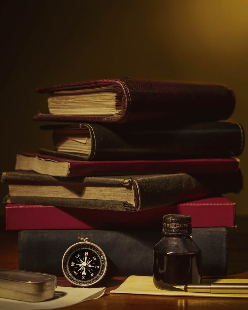 Antique law books, an inkwell, a compass and a fountain pen on a wooden desk.